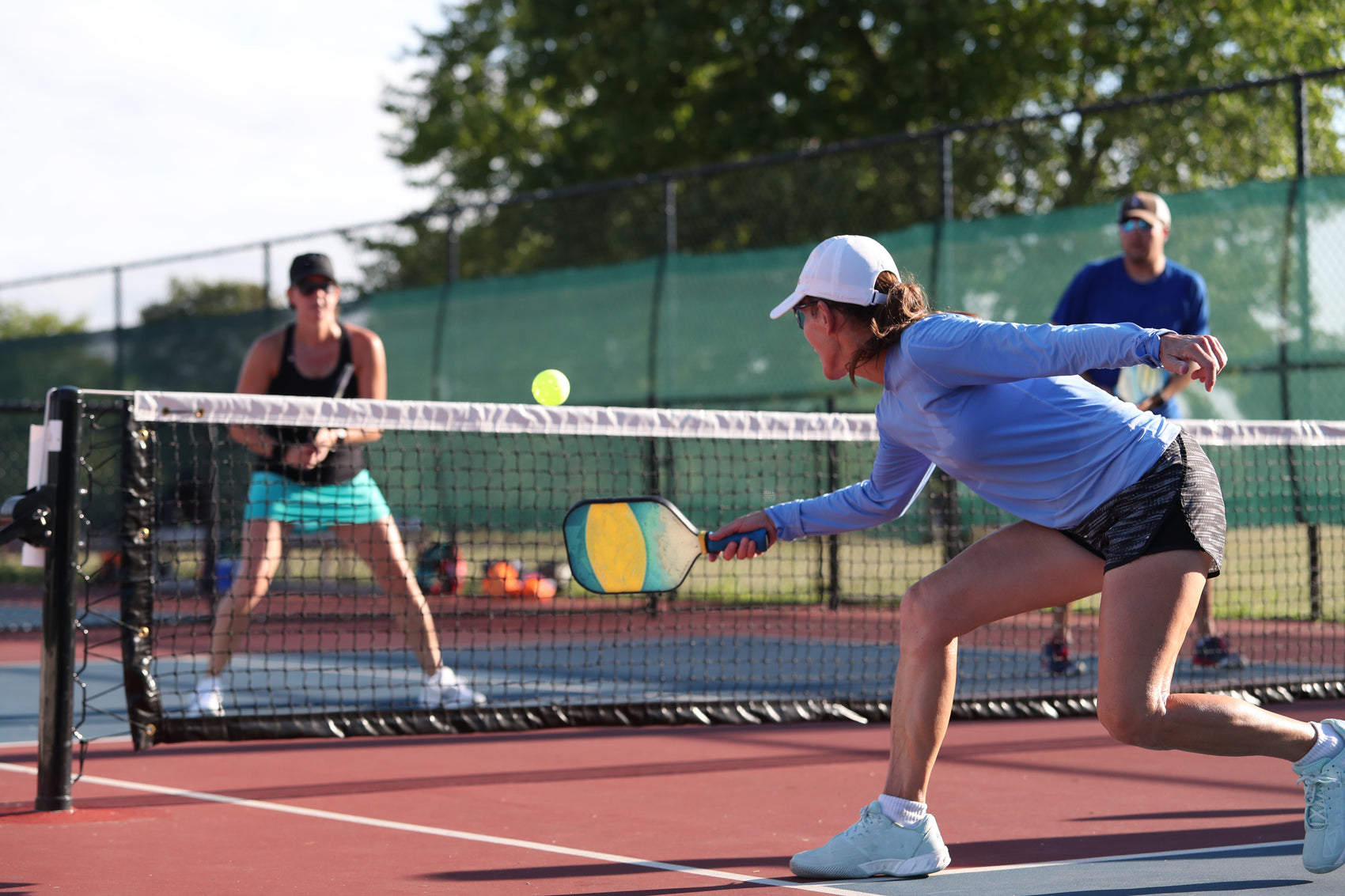 Pickleball player in action on a court with a net and other players in the background.