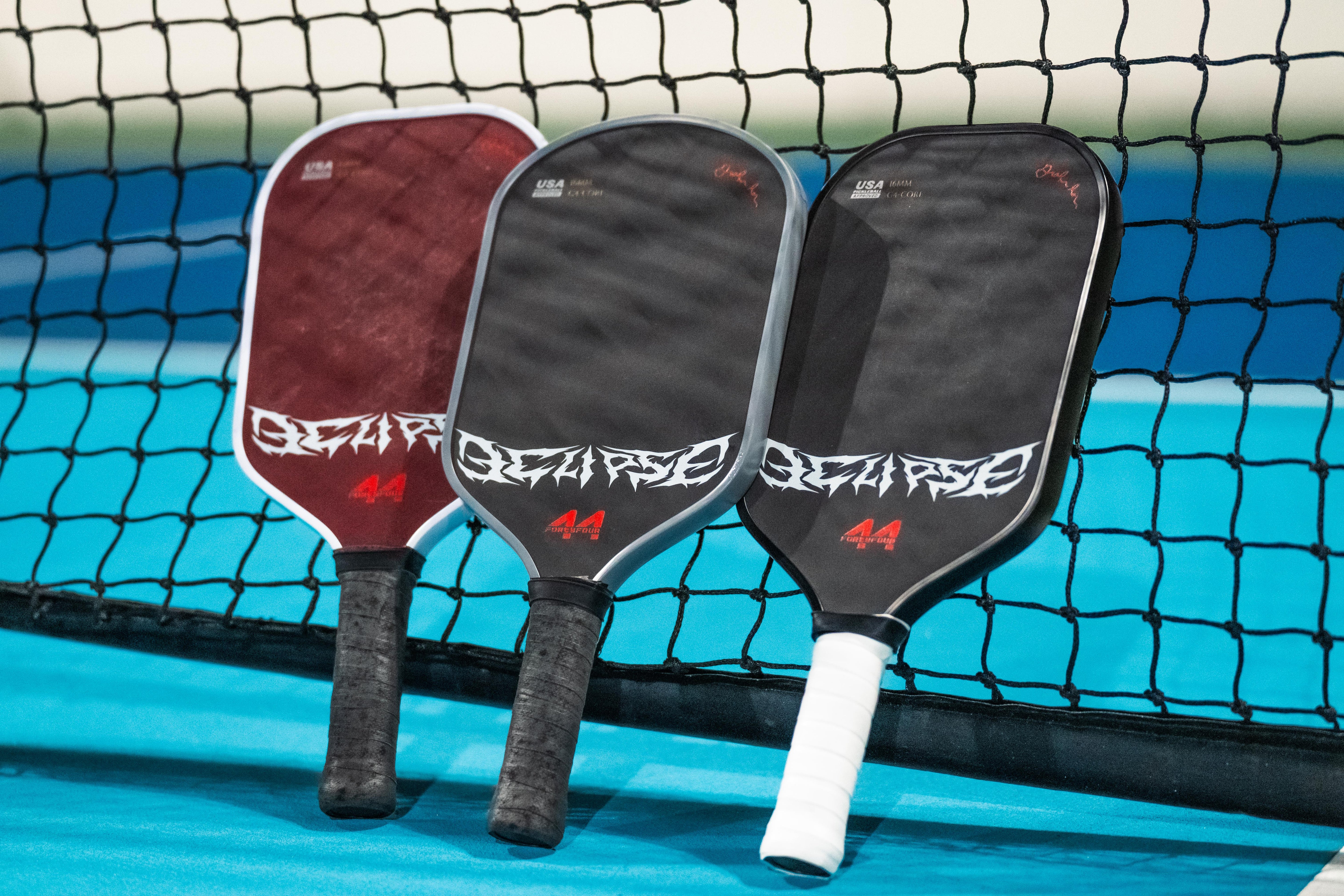 Three custom pickleball paddles leaning against a net on a blue court