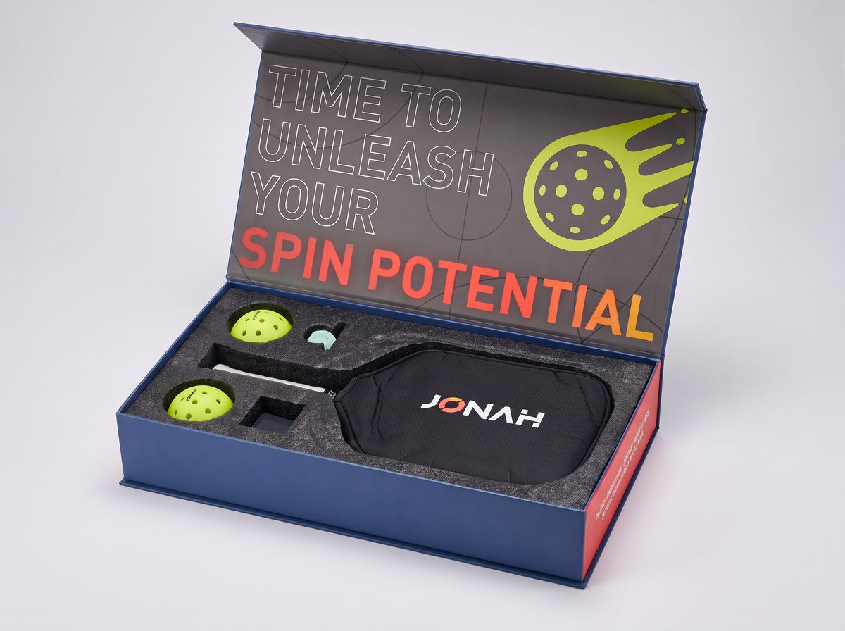 Custom presentation box for a complete pickleball set, open: printed inner lid, foam tray with two paddles, two balls, an overgrip and a paddle eraser