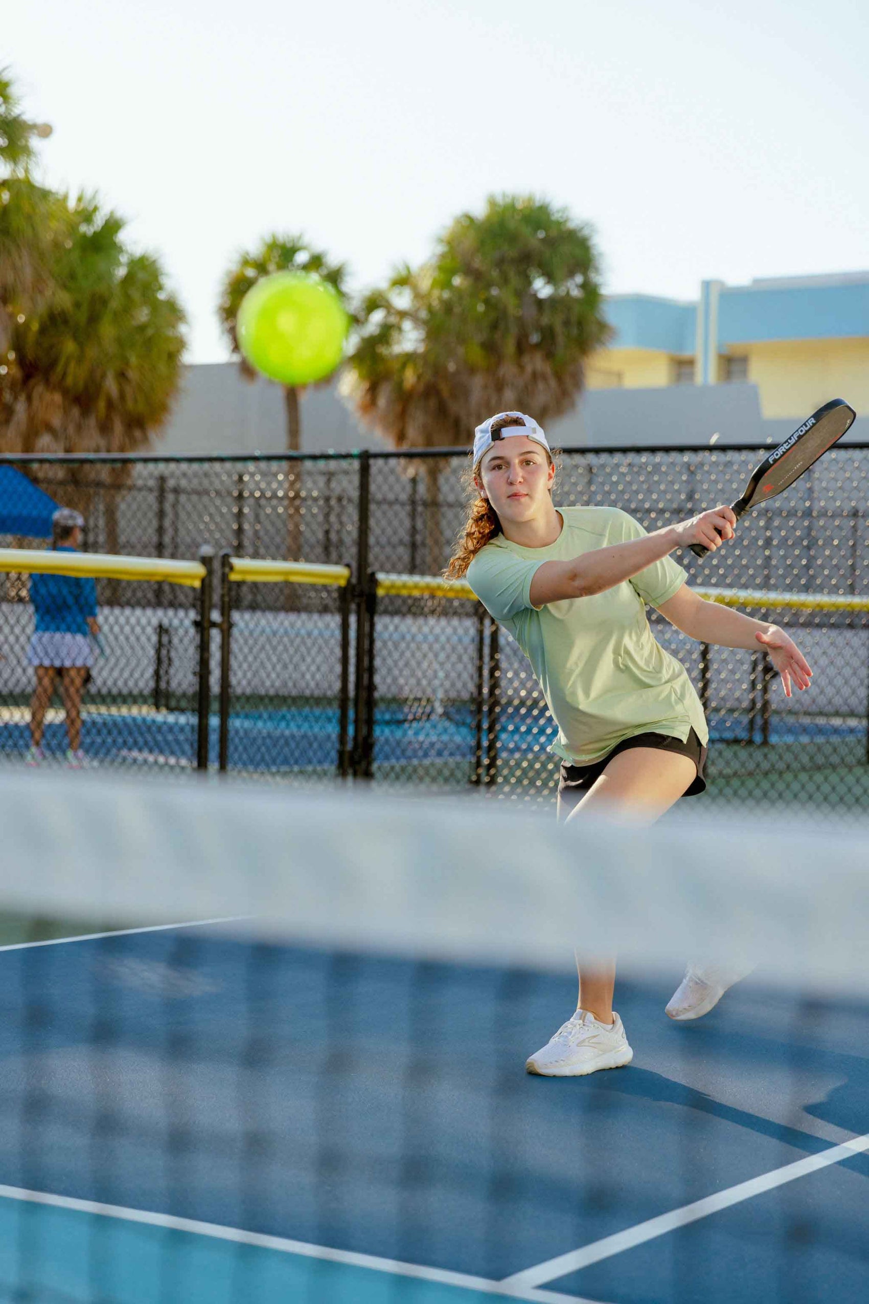 Woman playing pickleball on an outdoor court with a green ball and paddle.