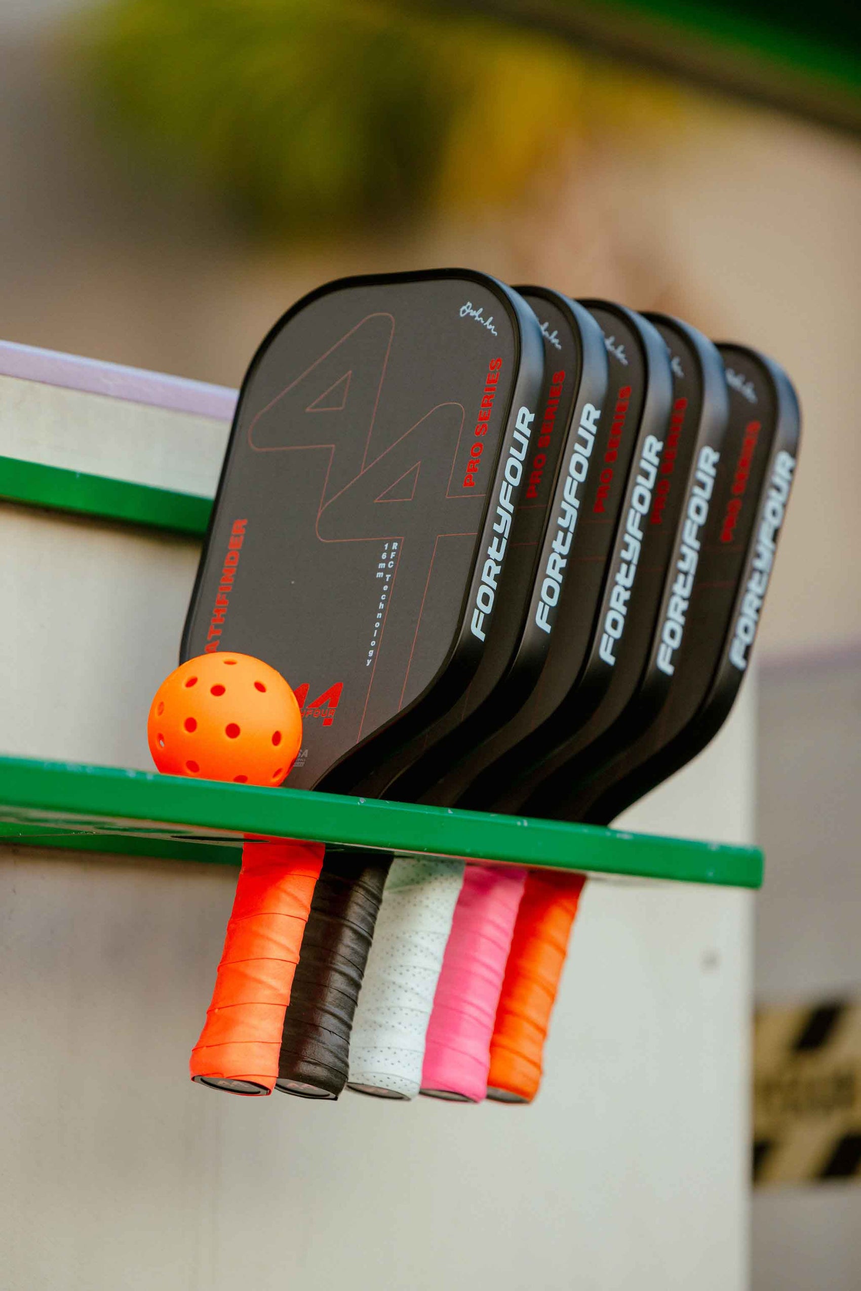 Set of pickleball paddles with colorful handles on a green rack.